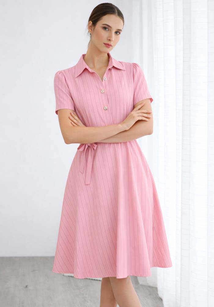 Ροζ midi φόρεμα με κάθετες ρίγες, κοντά μανίκια, χρυσά κουμπιά και υφασμάτινη ζώνη στη μέση.